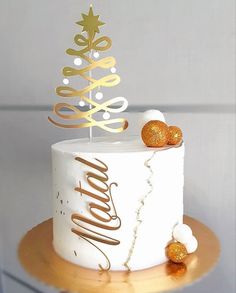 a white cake with gold decorations and a merry christmas tree on top, sitting on a wooden stand