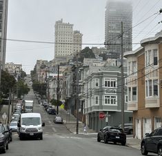 cars are parked on the street in front of tall buildings and power lines above them