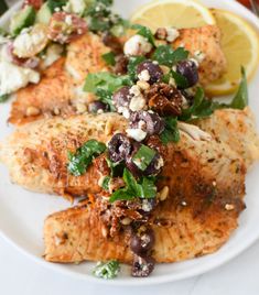 a white plate topped with fish covered in olives and garnished with feta cheese