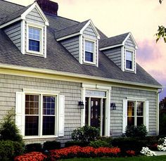 a gray house with white trim and two windows on the front, surrounded by flowers