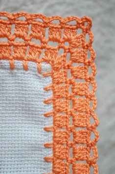 an orange and white crochet piece is on the edge of a table cloth