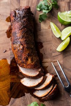 sliced meat sitting on top of a wooden cutting board next to limes and cilantro