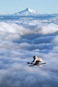 the skier is flying high above the clouds in the sky with his skis on