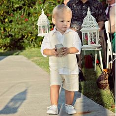 a little boy walking down the sidewalk with a cup in his hand and some white lanterns behind him