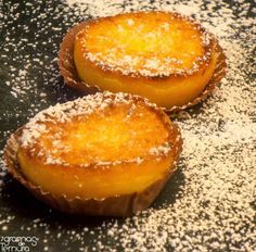 two pastries covered in powdered sugar sit on a black plate with white sprinkles