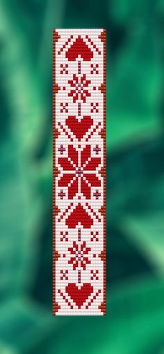 a red and white cross stitched bookmark hanging from a string on a green background