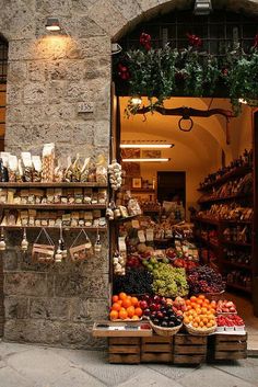 an open market with fruits and vegetables on display in front of a stone building that has arched doorways