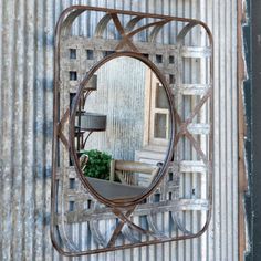 a mirror hanging on the side of a metal wall with a plant in it and a lamp next to it