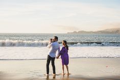 a man and woman standing on the beach holding hands with waves crashing in the background