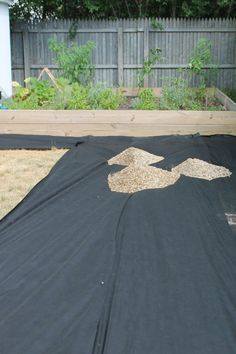 a black tarp covered in sand next to a wooden fence and yard with trees