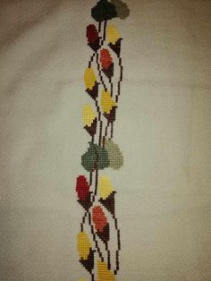 a cross - stitch design with leaves and flowers on white fabric, in the shape of a tree