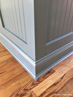 the corner of a room with wood flooring and gray painted paneling on the walls