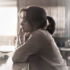 a woman sitting at a table with a book in her hand and looking off into the distance