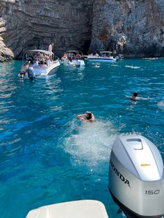 people swimming in the water near boats and cliffs