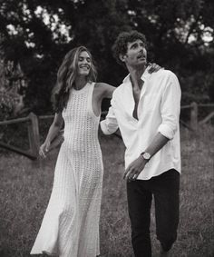 black and white photograph of man and woman walking in field with trees in the background