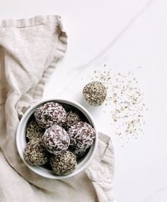 a bowl filled with chocolate covered donuts on top of a white table cloth next to two balls of sprinkled sugar