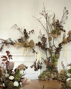 an arrangement of flowers and branches on display in a room with white paneled walls