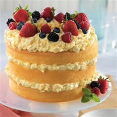 a three layer cake with strawberries and blueberries on top is sitting on a plate