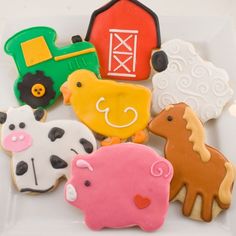 decorated cookies in the shape of farm animals and tractors on a white plate with a red barn