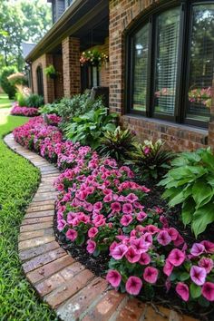 pink flowers line the side of a brick house with green grass and trees in the background