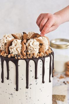 someone is decorating a cake with white frosting and cookies on the top layer