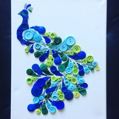 a peacock made out of buttons sitting on top of a piece of white paper with blue and green buttons