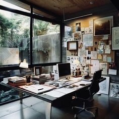 an office with lots of pictures on the wall and desk in front of large windows