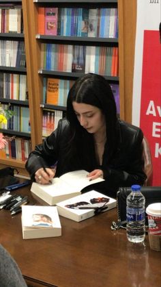 a woman sitting at a table with an open book in front of bookshelves