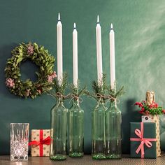 christmas decorations with candles and presents on a table next to a green wall, decorated for the holiday season