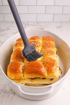 a white bowl filled with hot dogs covered in cheese and bread, being held by a plastic spatula