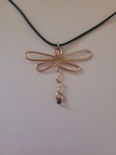 a gold dragonfly pendant is hanging from a green cord on a white surface with a black bead