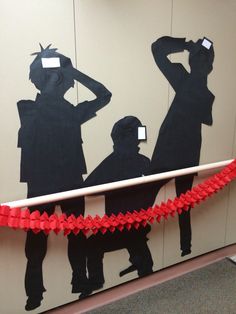 some people are standing in front of a wall with paper cutouts on it and tape