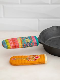 a cast iron skillet and an oven mitt on a white countertop next to a colorful pot holder