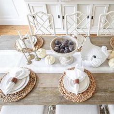 the table is set with plates, silverware and white pumpkins on it's placemats