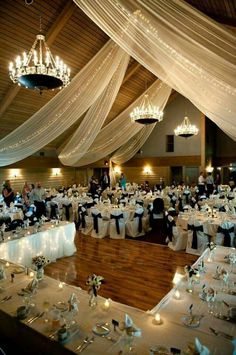 a room filled with lots of tables covered in white cloths and chandeliers