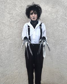 a man with black hair and suspenders standing in front of a wall