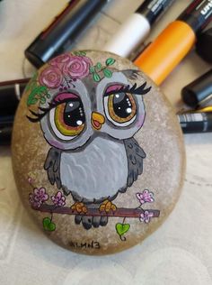 a rock with an owl painted on it sitting next to pens and markers in the background