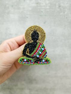 a hand holding a small beaded buddha brooch