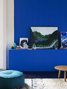 a living room with blue walls and art on the wall, coffee table and ottoman