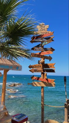 a wooden sign sitting on the side of a beach next to the ocean in front of a palm tree