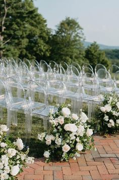 rows of clear acrylic chairs with white flowers and greenery on the ground