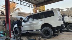 two men standing next to a white suv in a garage with the hood up on