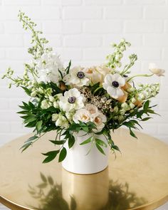 a vase filled with white flowers sitting on top of a gold table next to a brick wall