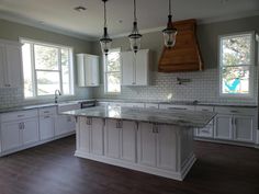 an empty kitchen with white cabinets and marble counter tops, wood flooring and pendant lights