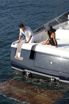 two people standing on the back of a boat in the water near another person sitting down