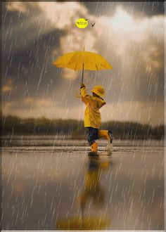 a little boy in yellow raincoat holding an umbrella over his head while walking on the beach