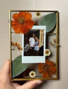 a person holding up a photo frame with flowers on it