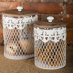 two white metal canisters with wooden lids on a brown table next to a brick wall