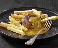 a black plate topped with french fries and a piece of meat covered in sauce next to a fork