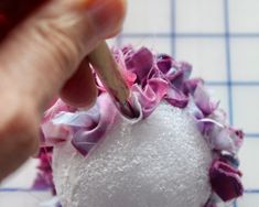 a person is using a pencil to decorate a white ball with pink and purple flowers